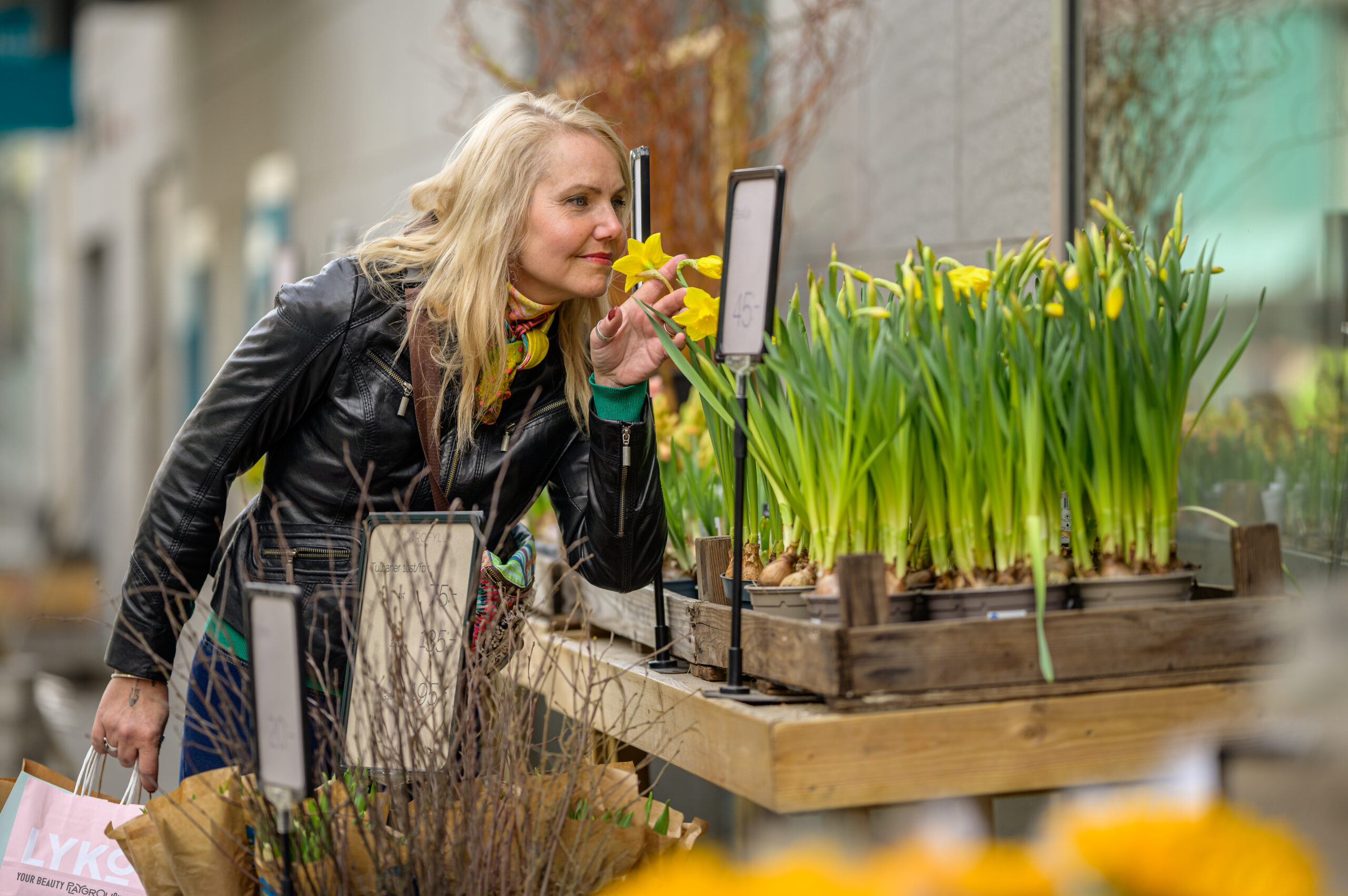 En blond kvinna luktar på gula påskliljor utanför en blomsteaffär